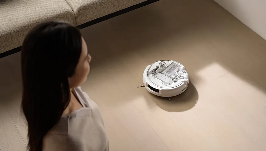 Woman standing near the DJI Romo robot vacuum as it moves across a light-colored floor
