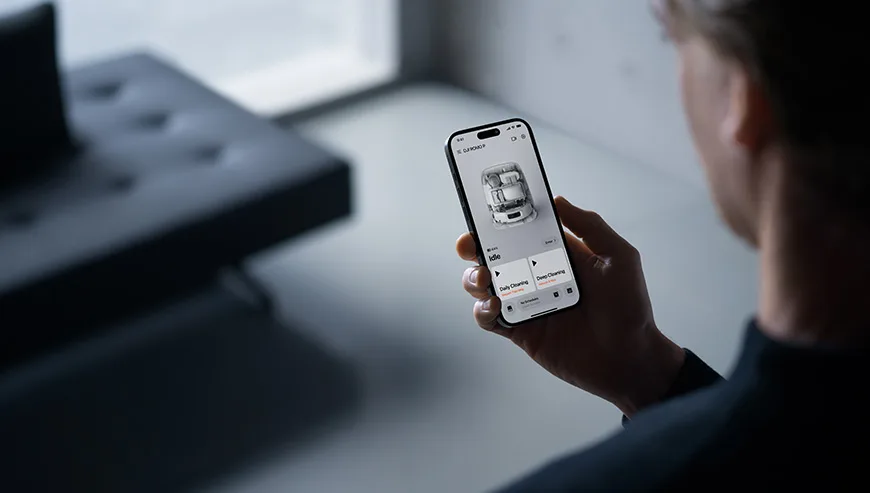 Man holding a smartphone with the DJI ROMO robot vacuum control app on the screen
