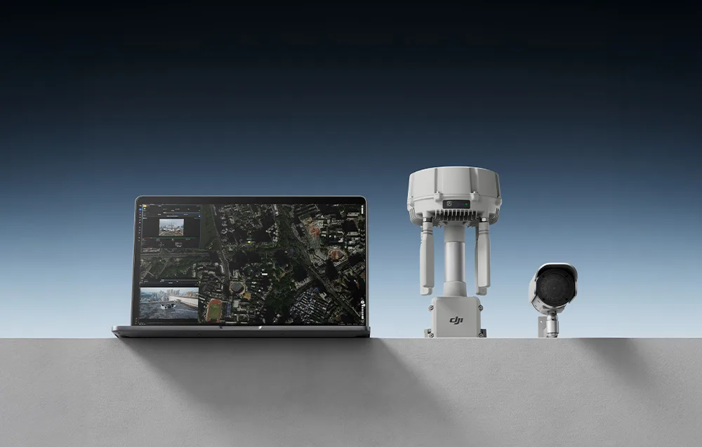 Otwarty laptop wyświetlający mapę, stacja DJI O4 Ground Station i kamera IP na szarym podeście na ciemnym tle