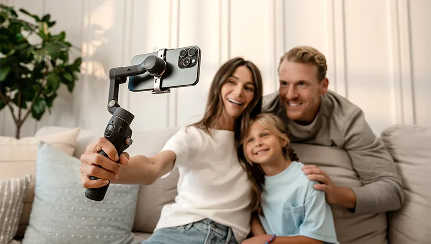 Rodzina robiąca selfie na kanapie w salonie za pomocą telefonu na gimbalu DJI Osmo Mobile 8